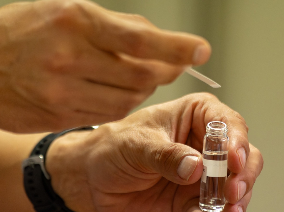 Hand holding a clear vial sample of Massoia lactone